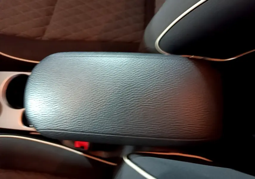 Détail de l'accoudoir central en cuir noir avec surpiqûres blanches dans l'habitacle d'une Fiat 500X gris foncé.