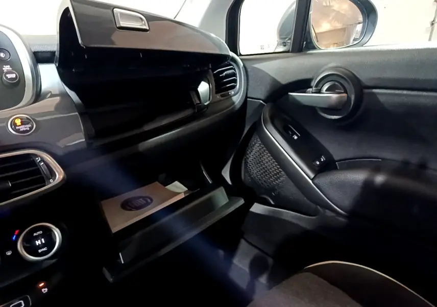 Intérieur côté passager du Fiat 500X gris foncé, avec boîte à gants ouverte et commandes de porte visibles.