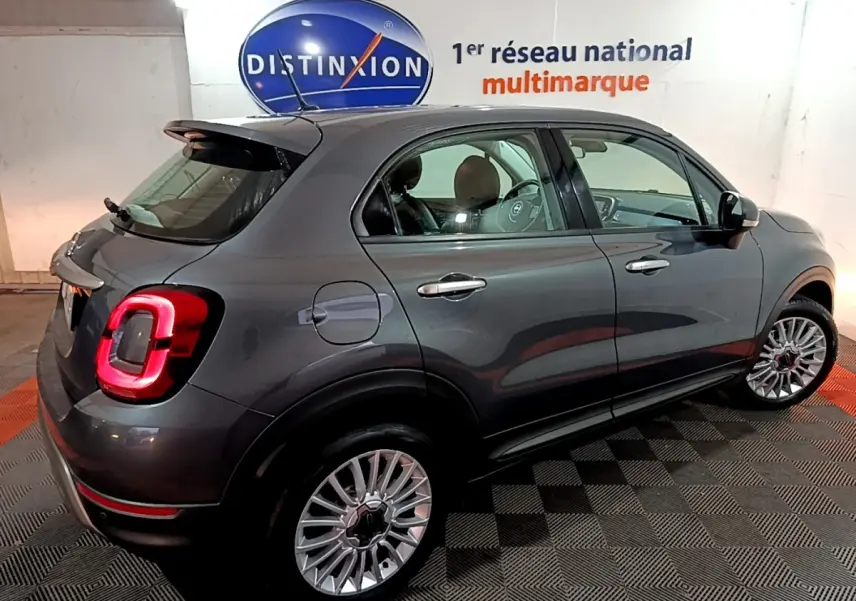 Vue 3/4 arrière droite d'une FIAT 500X gris foncé avec feux arrière allumés dans un showroom intérieur.
