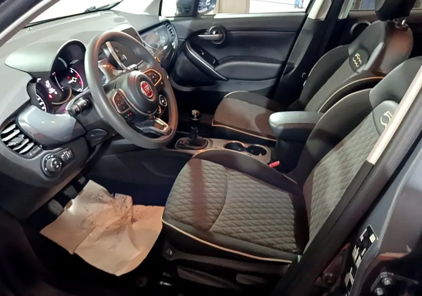 Intérieur avant droit de la FIAT 500X gris foncé, montrant sièges tissu, volant multifonctions et levier de vitesse manuel.