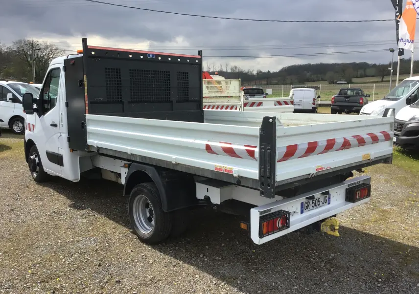 Vue 3/4 arrière droite d’un Renault Master blanc avec benne et coffre, marquages réfléchissants rouges et roues jumelées.
