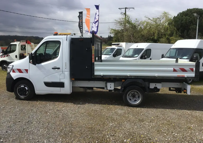 Vue de profil côté gauche d’un Renault Master blanc avec benne et coffre noir, équipé de roues jumelées et bandes réfléchissantes rouges.