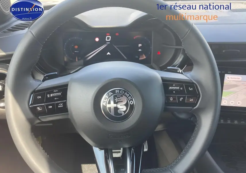 Vue centrée sur le volant cuir de l'Alfa Romeo Junior 1.2 hybride 2026 avec tableau de bord numérique et écran tactile.