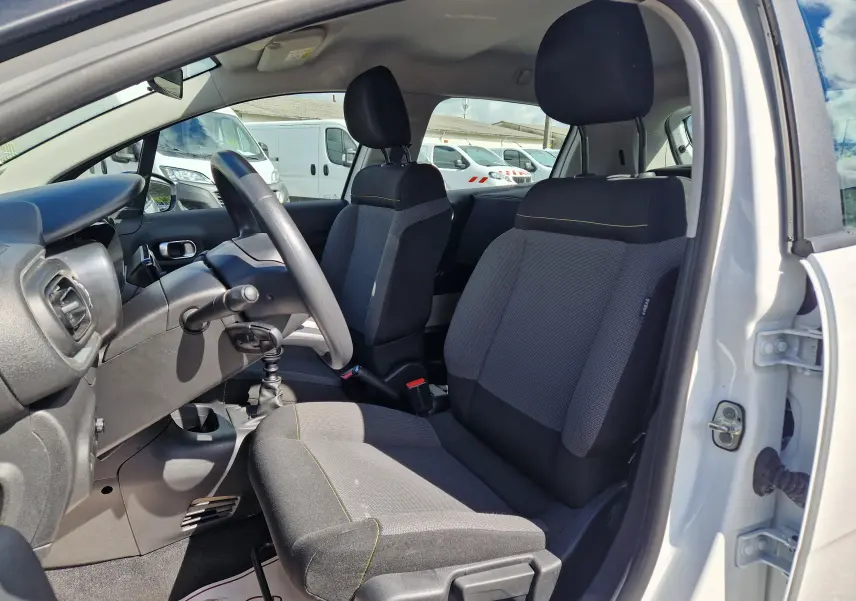 Vue intérieure côté conducteur d'une Citroën C3 Société blanche 2021, sièges tissu gris avec surpiqûres jaunes et volant noir.