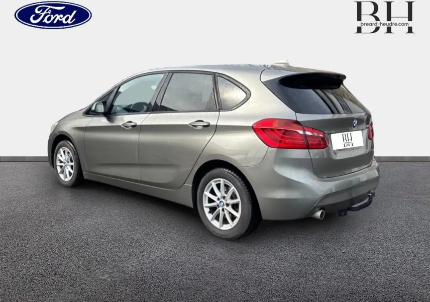 BMW Série 2 Active Tourer 216dA grise vue 3/4 arrière droit, avec jantes alu et attelage visible.