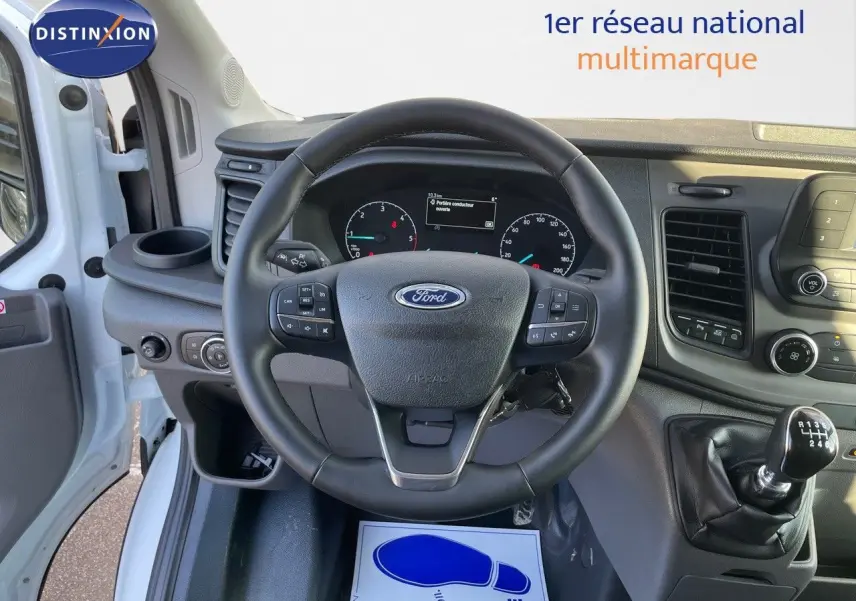 Vue intérieure centrée sur le volant et le tableau de bord du Ford Transit Fourgon blanc 2023 avec boîte manuelle.