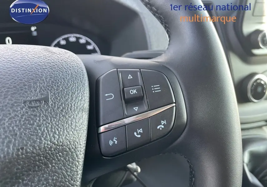 Gros plan sur les commandes au volant noir du Ford Transit Fourgon blanc, avec tableau de bord et console en arrière-plan.