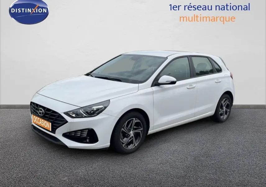 Hyundai i30 blanc nacré vue 3/4 avant droit, compacte 5 portes avec jantes alliage et calandre noire distinctive.