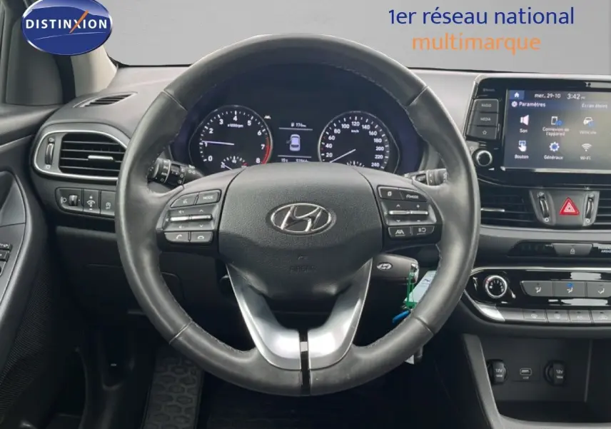 Vue intérieure centrée sur le volant noir de la Hyundai i30 2023 avec tableau de bord et écran tactile visible.