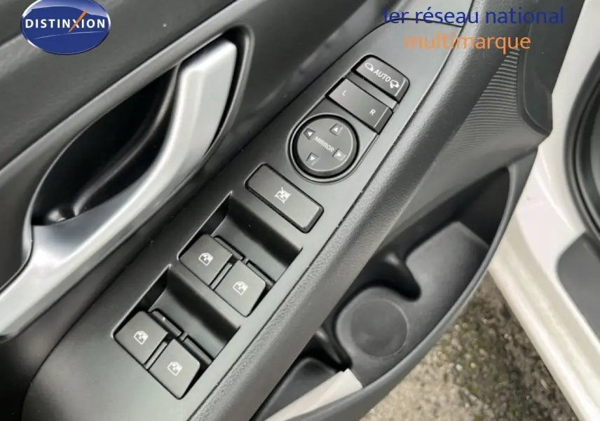 Gros plan sur la commande des vitres et rétroviseurs côté conducteur d'une Hyundai i30 blanc nacré 2023.