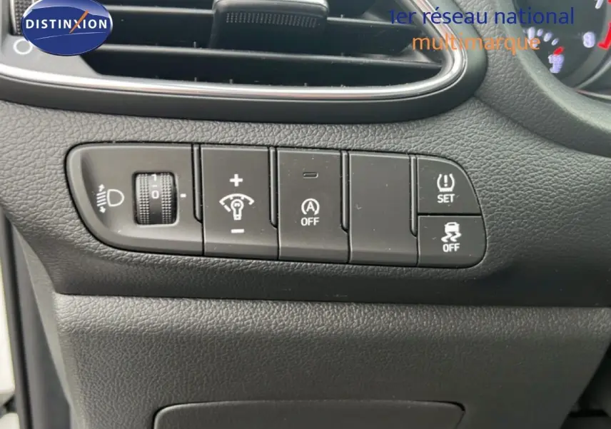 Gros plan sur les commandes de réglage d’éclairage et d’assistance du tableau de bord d’une Hyundai i30 blanche nacrée 2023.