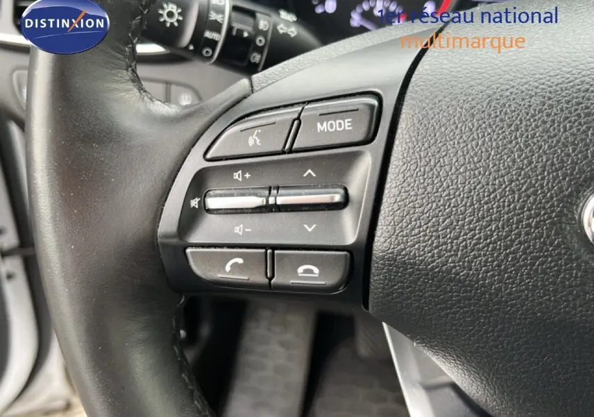 Gros plan sur les commandes gauche du volant noir d'une Hyundai i30 blanche nacrée, mettant en valeur les boutons multifonctions.