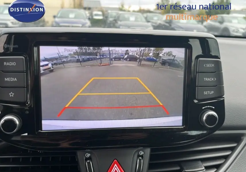 Écran central de la Hyundai i30 blanc nacré 2023 montrant la caméra de recul avec lignes de guidage colorées.