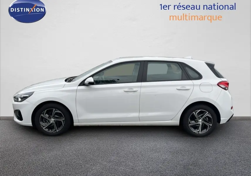 Vue de profil côté gauche d'une Hyundai i30 blanche nacrée 5 portes, avec jantes alliage et lignes épurées.