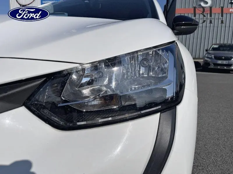 Gros plan sur le phare avant droit d'une Peugeot 208 AFFAIRE blanc banquise 2022, soulignant ses détails lumineux.