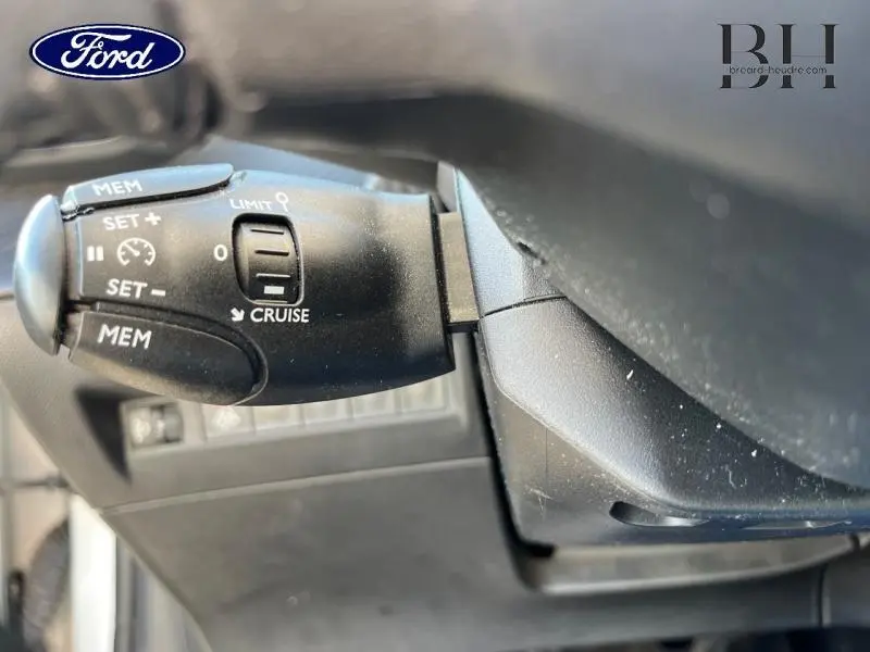 Gros plan sur la commande de régulateur de vitesse noire dans l'habitacle d'une Peugeot 208 Affaire blanc banquise.