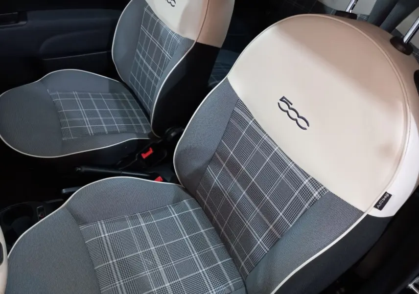 Gros plan sur les sièges avant gris à motif carreaux avec appuie-têtes blancs et logo 500 brodé dans l’habitacle d’une Fiat 500.