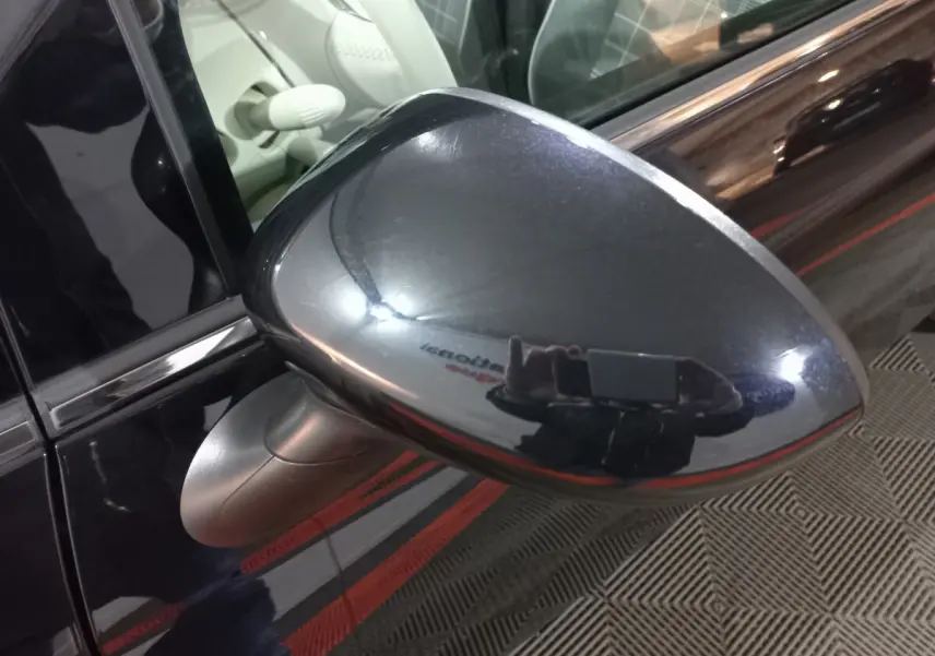 Gros plan sur le rétroviseur côté conducteur noir brillant de la FIAT 500 Lounge 2018, avec reflet de l'environnement.