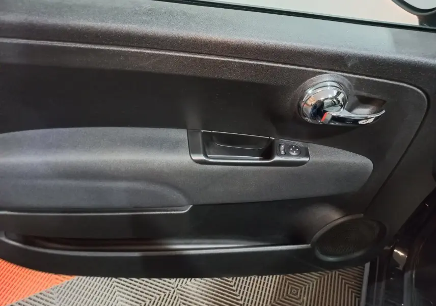 Vue rapprochée de la porte intérieure côté conducteur noire de la FIAT 500 Lounge avec poignée chromée et commandes électriques.