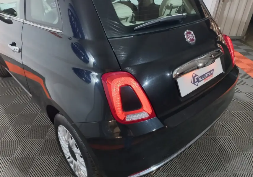 Vue 3/4 arrière droite d'une FIAT 500 noire 2018 avec feux arrière allumés et jantes argentées sur sol damier.