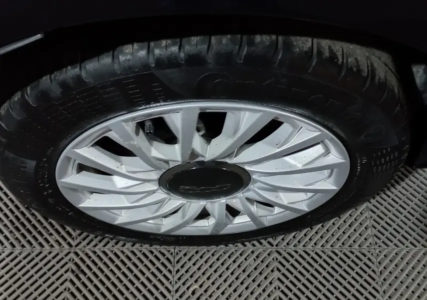 Gros plan sur la roue avant droite d’une FIAT 500 noire, mettant en valeur la jante argentée au design en étoile.