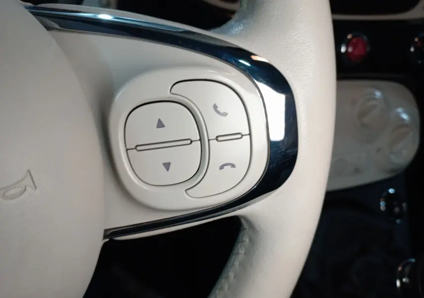 Gros plan sur les commandes blanches du volant cuir côté gauche de la Fiat 500 Lounge noire de 2018.