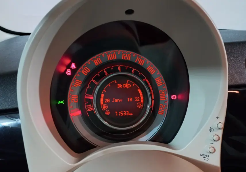 Gros plan sur le tableau de bord circulaire de la Fiat 500 noire, avec affichage digital rouge et indicateurs lumineux allumés.