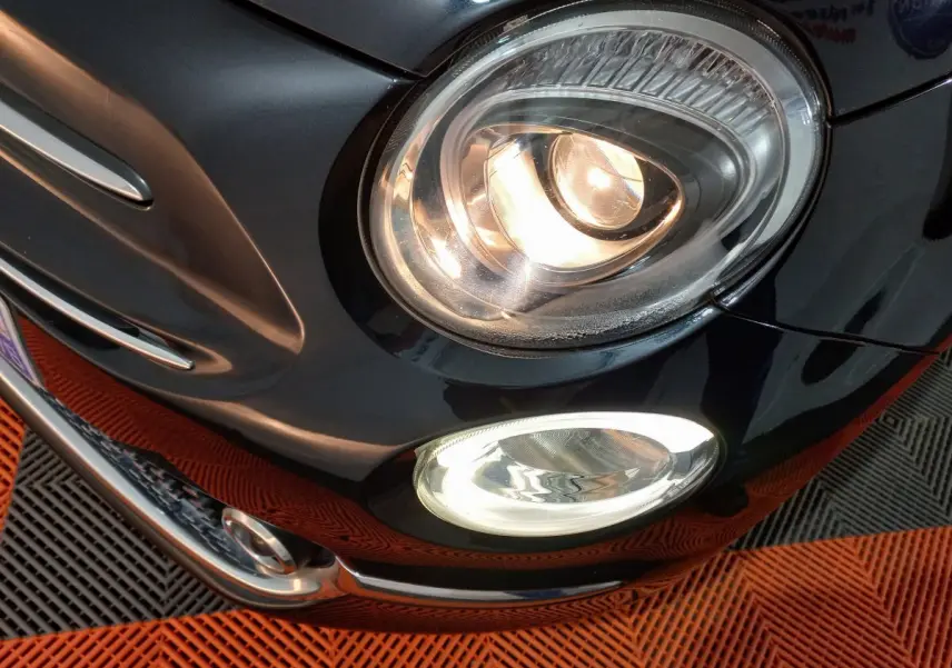 Gros plan sur l'avant droit noir d'une Fiat 500 2018, mettant en valeur ses phares allumés et antibrouillards.