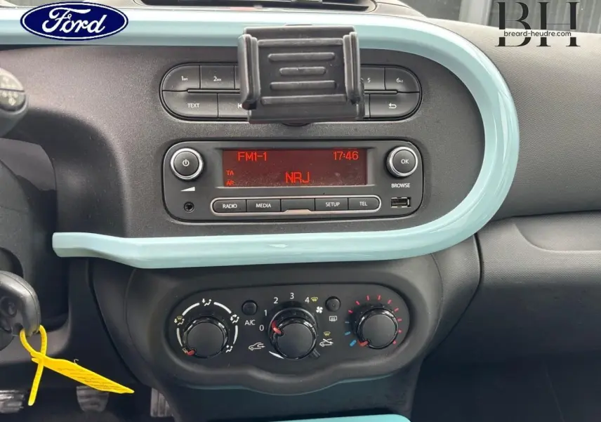 Tableau de bord intérieur d'une Renault Twingo bleu dragée 2014, avec commandes clim manuelle et radio affichant NRJ.
