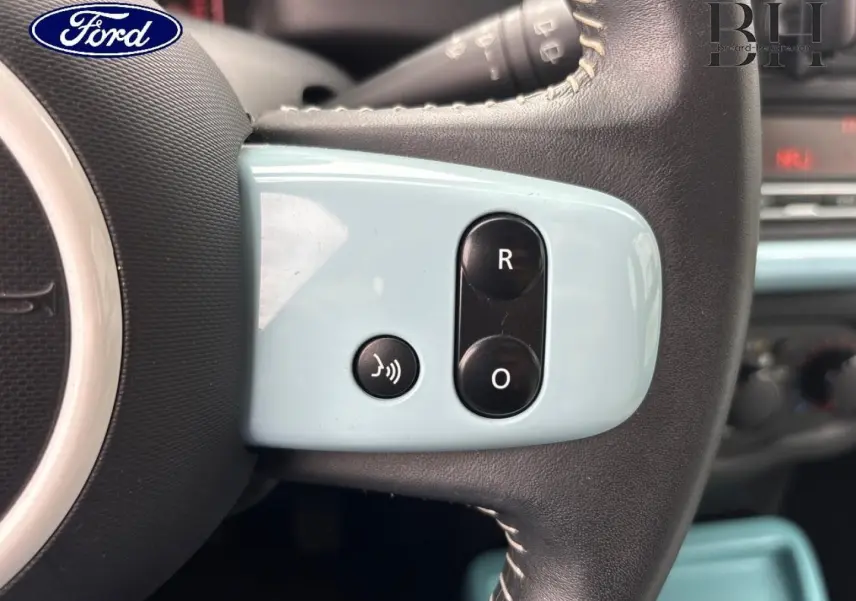 Gros plan sur les commandes bleues du volant d’une Renault Twingo 2014 Bleu Dragée, côté gauche.