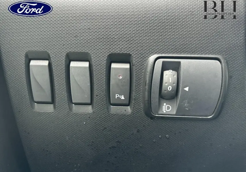 Gros plan sur les commandes de réglage des phares et de l'aide au stationnement d'une Renault Twingo bleu dragée.