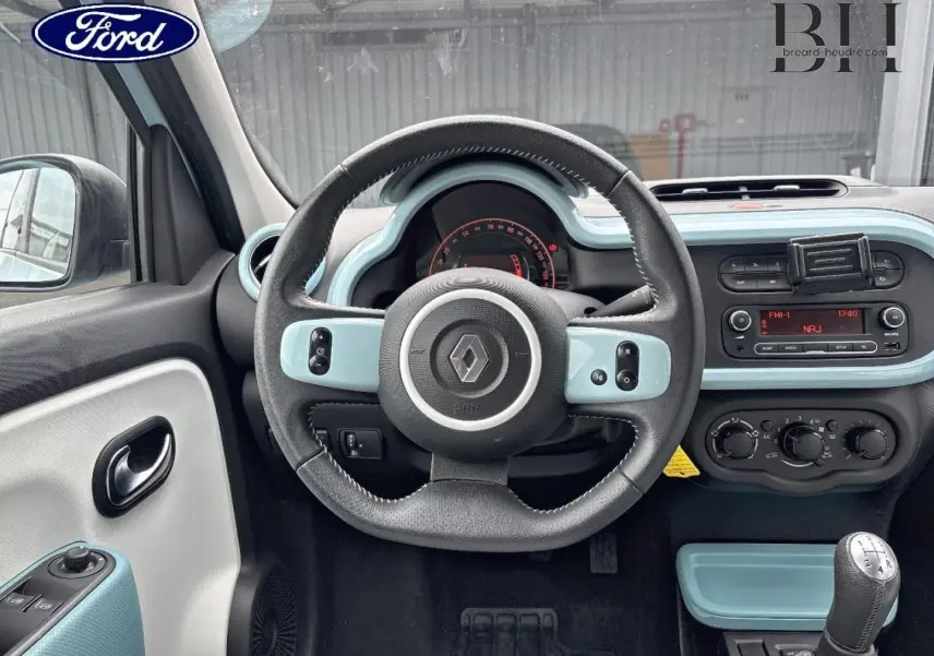 Vue intérieure centrée sur le volant et le tableau de bord bleu dragée de la Renault Twingo 2014 avec boîte manuelle.