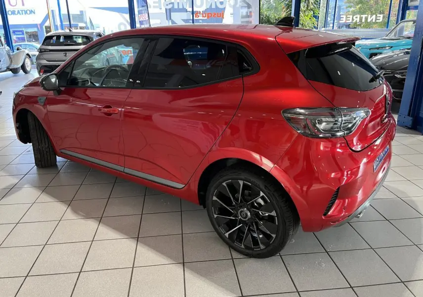 Renault Clio 2024 rouge vue 3/4 arrière droit avec jantes noires et vitres surteintées en showroom.