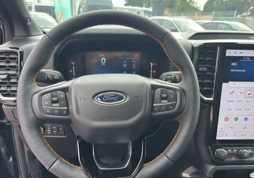 Vue intérieure centrée sur le volant noir du Ford Ranger 2025 Wildtrak Plus avec tableau de bord digital et écran tactile.