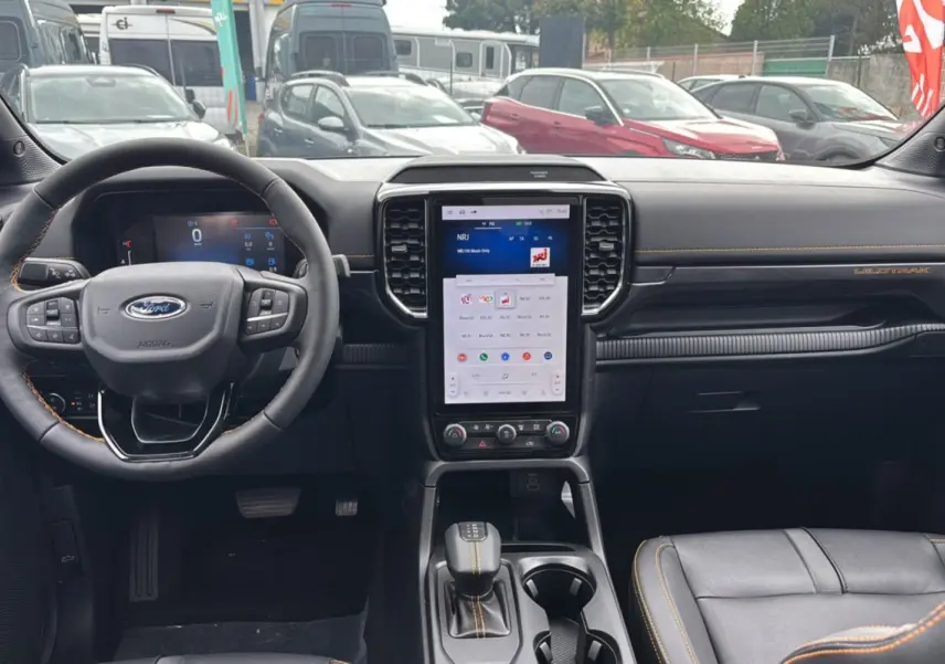 Vue intérieure du tableau de bord du Ford Ranger Wildtrak Plus 2025 noir agate avec écran tactile vertical et coutures orange.