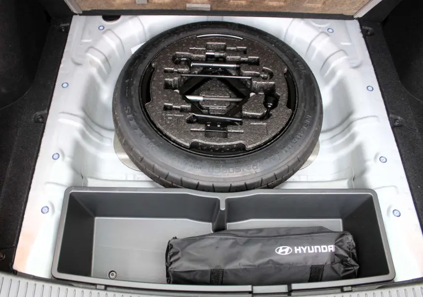 Vue plongeante sur la roue de secours et le rangement du coffre d'une Hyundai i30 SW 2024 couleur argent scintillant.
