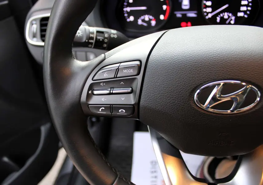 Gros plan sur le volant cuir noir de la Hyundai i30 SW 2024 avec commandes audio intégrées côté gauche.