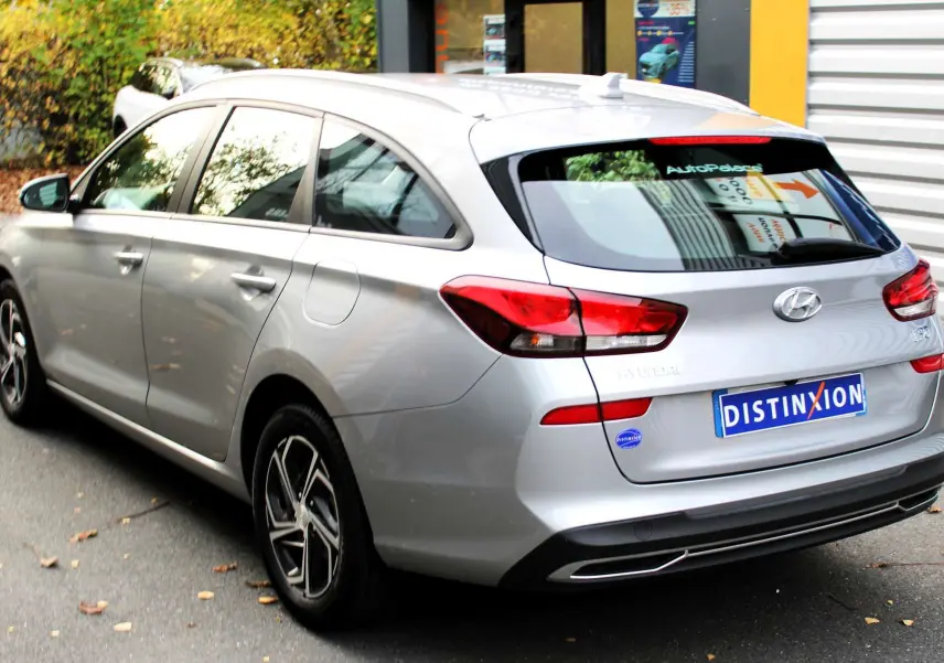 Intérieur côté conducteur de la Hyundai i30 SW 2024 en Shimmering Silver, sièges tissu gris et noir, volant et levier manuel visibles.