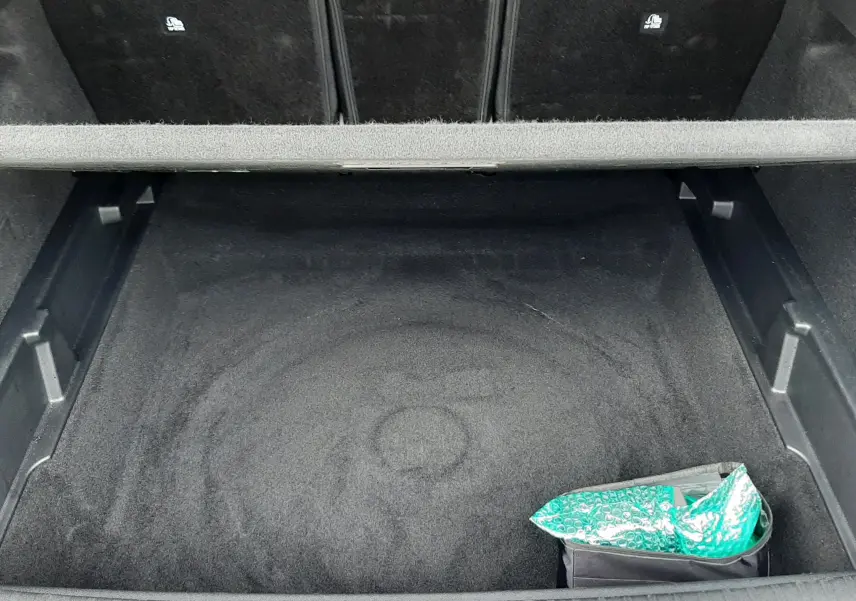 Vue plongeante sur le coffre spacieux et propre d’un Peugeot 3008 III HYBRID 145 ALLURE e-DSC6, avec un sac vert dans un coin.