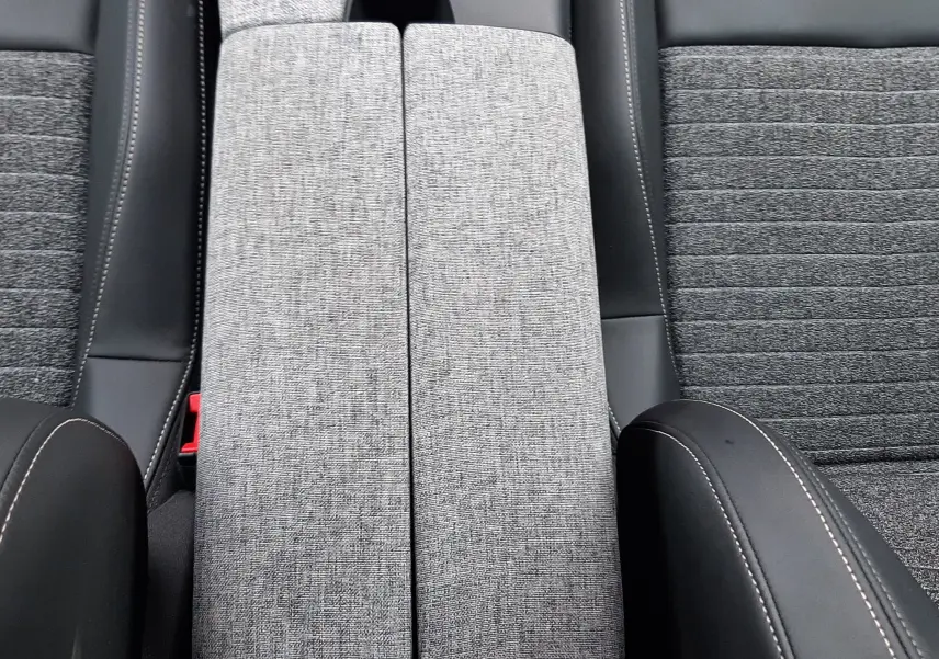 Vue plongeante sur l'accoudoir central gris tissu et les sièges noirs avec surpiqûres blanches du Peugeot 3008 Hybrid 2025.