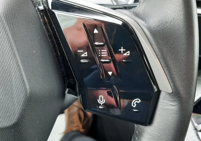 Gros plan sur les commandes tactiles noires du volant côté gauche du Peugeot 3008 Hybrid 2025, intérieur gris noir.