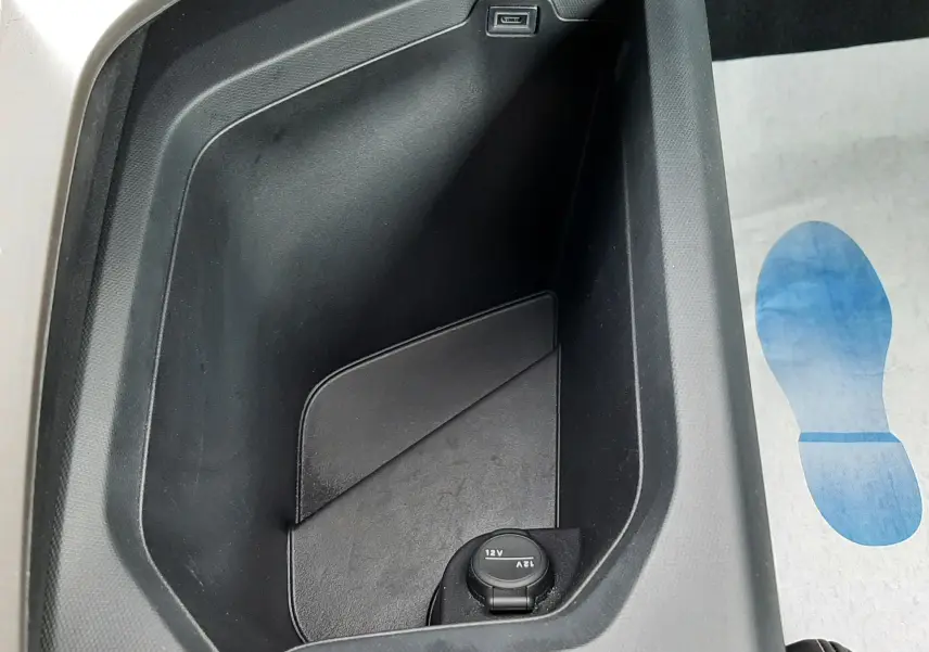 Vue rapprochée de la console centrale noire du Peugeot 3008 Hybrid 2025, avec prise 12V et port USB visible.