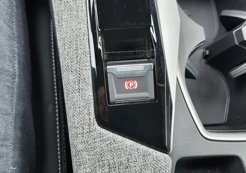 Gros plan sur le bouton de frein à main électronique rouge, entouré de garniture grise et console noire du Peugeot 3008 hybride 2025.