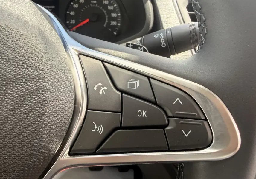 Gros plan sur les commandes multifonctions noires du volant réglable du Renault Trafic Fourgon blanc, tableau de bord en arrière-plan.