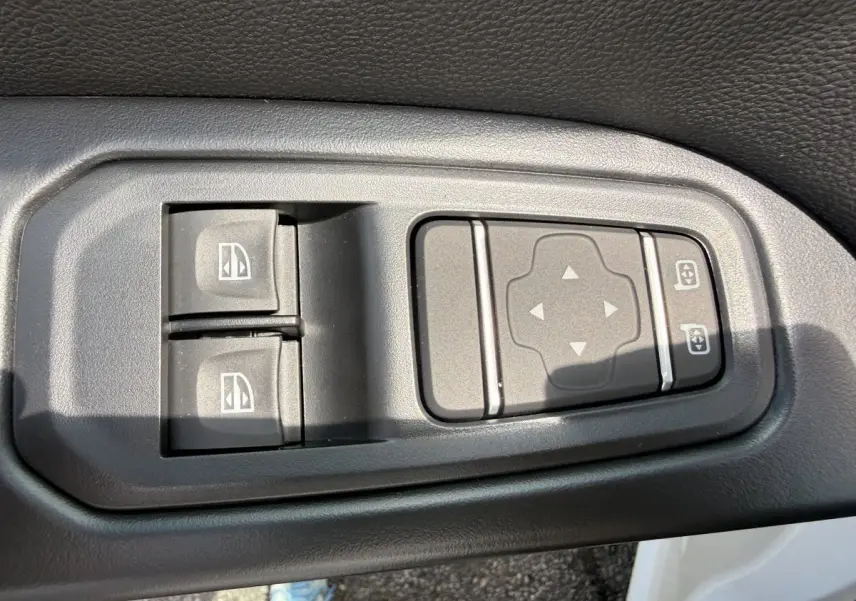 Gros plan sur les commandes de réglage des vitres et des rétroviseurs côté conducteur du Renault Trafic Fourgon blanc.