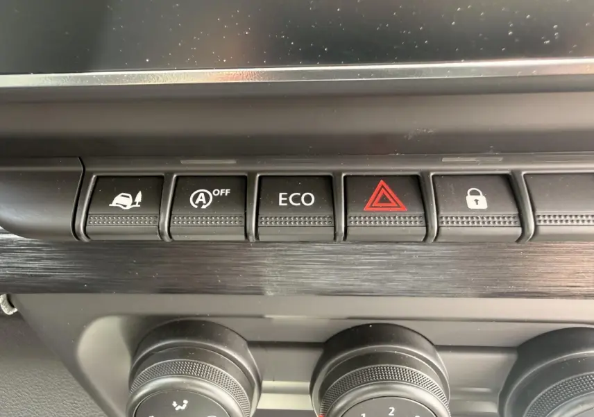 Gros plan sur la rangée de boutons de commande noirs et molettess du tableau de bord du Renault Trafic Fourgon blanc.