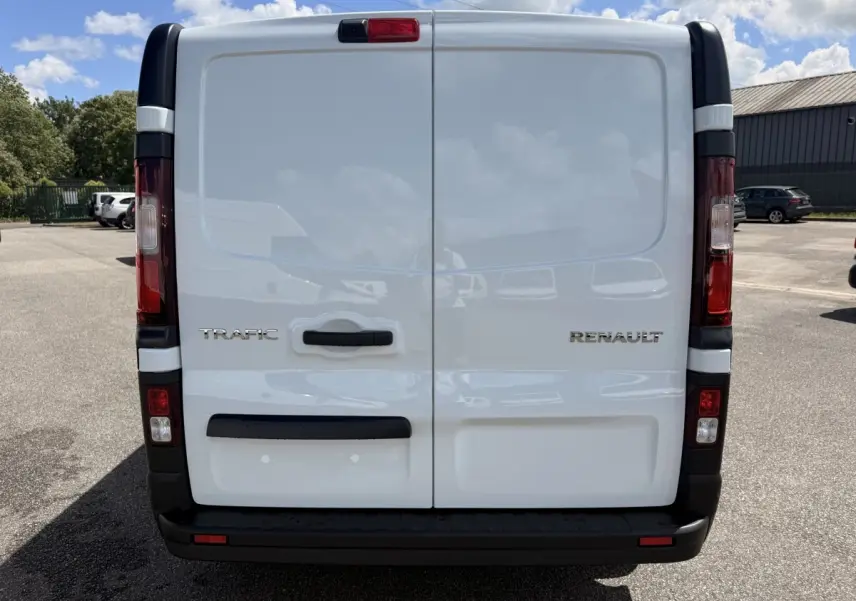 Vue arrière d’un Renault Trafic fourgon blanc avec portes battantes et feux arrière verticaux rouges et blancs.