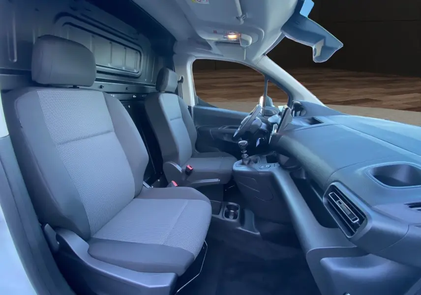 Intérieur du Peugeot Partner 2024 vu côté conducteur, sièges tissu gris et tableau de bord noir simple.