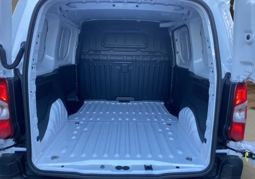 Vue arrière ouverte du Peugeot Partner blanc 2024 montrant la grande zone de chargement métallique vide et les feux arrière rouges.