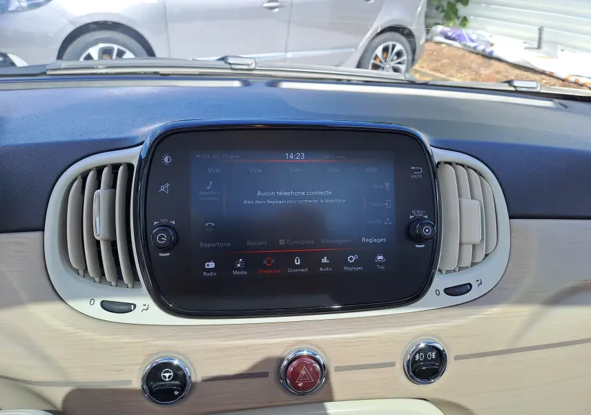 Tableau de bord clair de la Fiat 500 blanche, avec écran tactile central et aérateurs ovales beige.